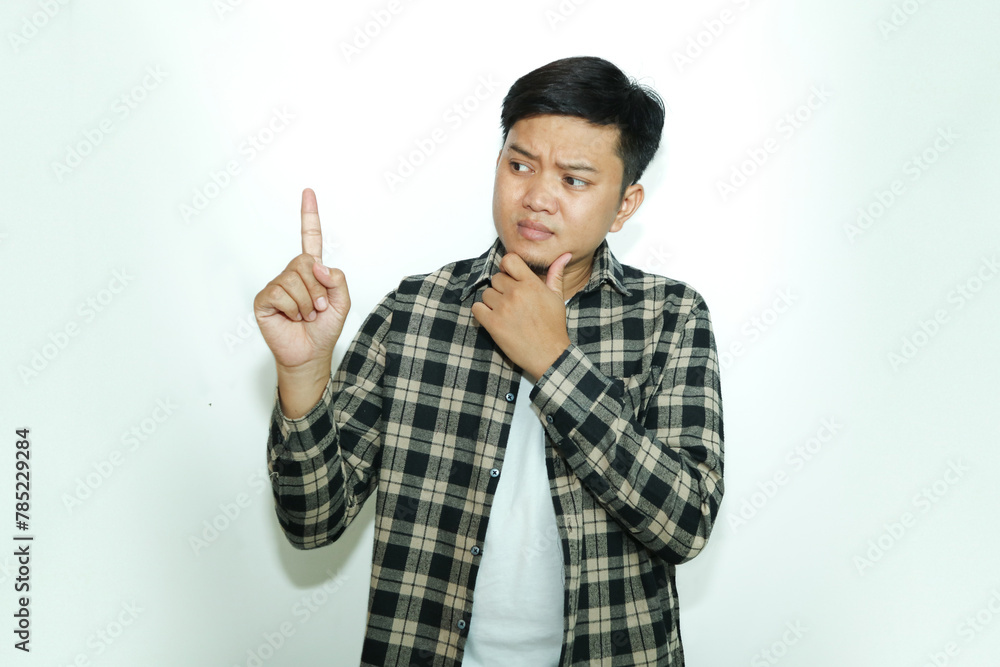 Young Asian man shows a curious facial expression while giving the one finger sign Young Asian man shows a curious facial expression while giving the one finger sign