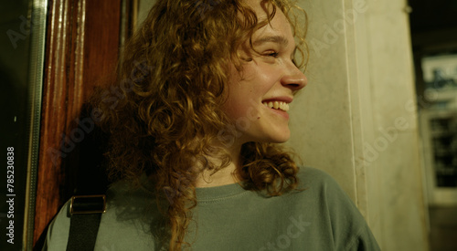 Close up view of an attractive young woman with curly hair looking forward, standing outdoors on a warm light of sunset.