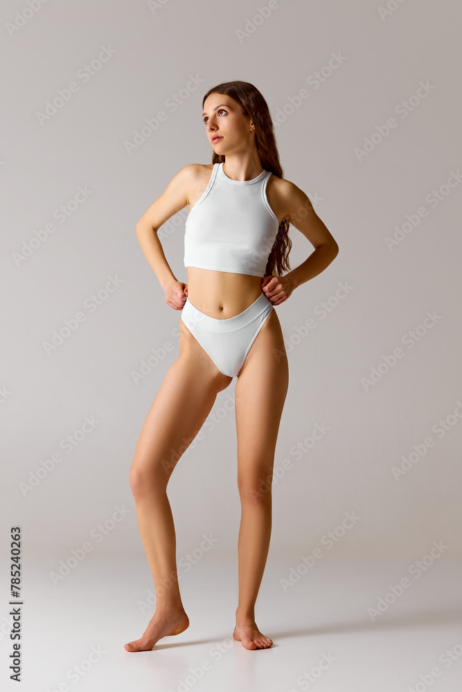 Fototapeta premium Full-length portrait of young, slim woman posing in underwear and looking away against white studio background. Concept of beauty and health, depilation, anti-cellulite program, dieting.