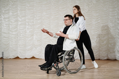 Long shot of young woman and mature man with disability in wheelchair performing modern dance on stage, copy space
