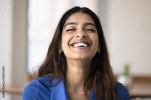 Happy relaxed carefree Indian woman laughing with closed eyes, showing perfectly white healthy teeth, smiling, posing indoors. Cheerful young 20s girl enjoying positive emotions