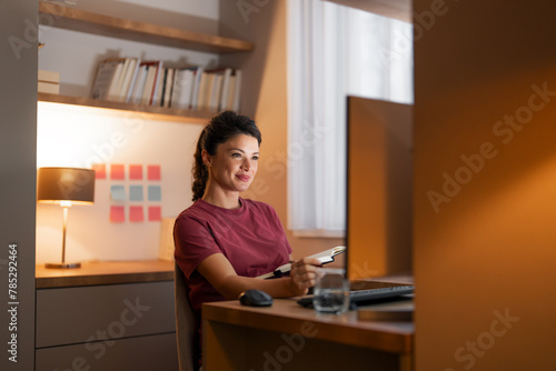 A smiling mid adult woman sitting at a desk and working on her computer from home © Jelena