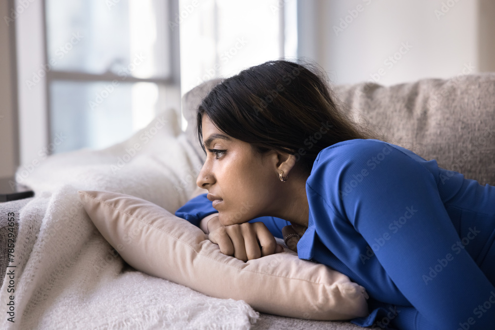 Sad young 20s Indian girl lying on home couch, looking away, thinking on problems, troubles, leaning chin on hand, looking away with apathy, feeling loneliness, fatigue, depression Sad young 20s Indian girl lying on home couch, looking away, thinking on problems, troubles, leaning chin on hand, looking away with apathy, feeling loneliness, fatigue, depression