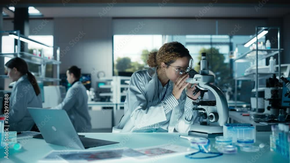 Beautiful Multiethnic Female Scientist Working on a Computer and Looking at a Sample in a Petri Dish Under a Microscope. Specialists Working in an Advanced Medical Research and Development Laboratory Beautiful Multiethnic Female Scientist Working on a Computer and Looking at a Sample in a Petri Dish Under a Microscope. Specialists Working in an Advanced Medical Research and Development Laboratory