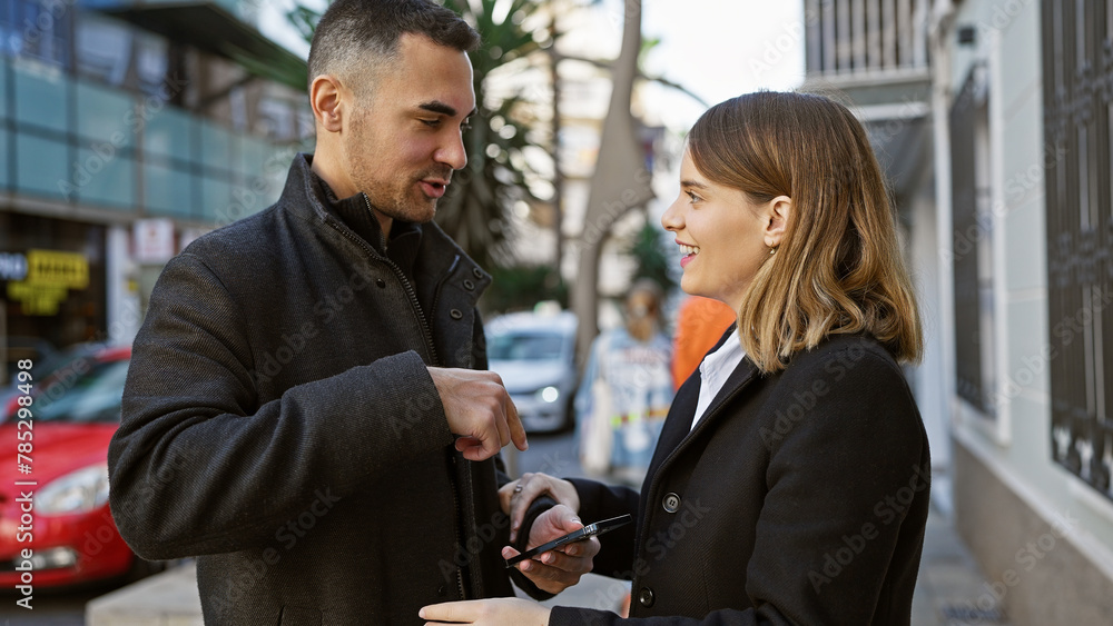 A man and woman share a moment on a city street, together looking at a mobile phone amidst an urban backdrop. A man and woman share a moment on a city street, together looking at a mobile phone amidst an urban backdrop.