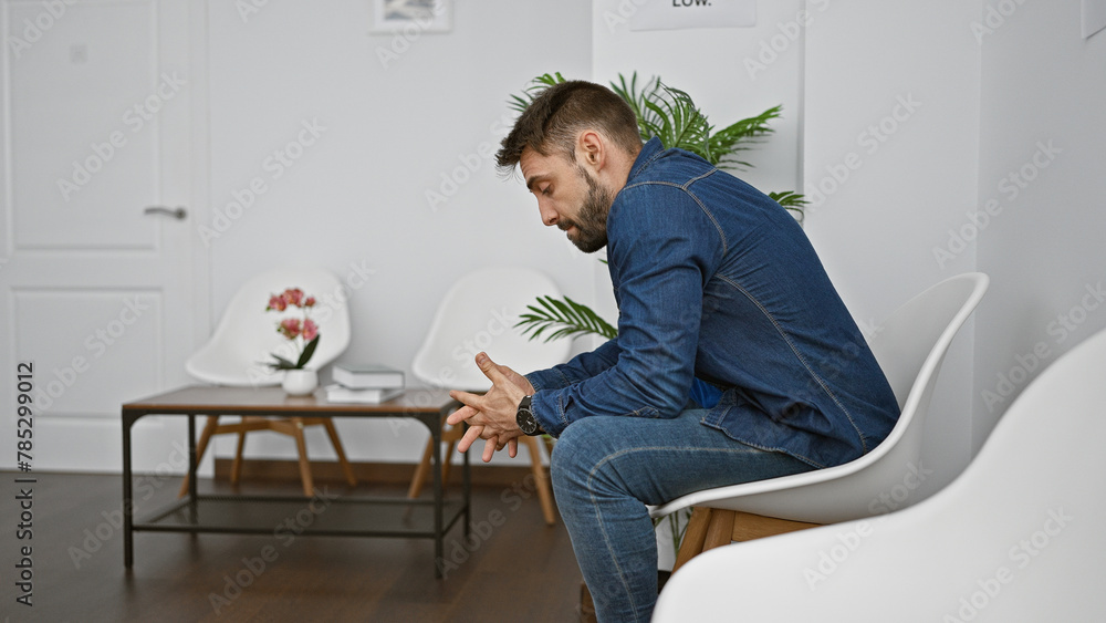 Young hispanic man sitting on chair looking upset at waiting room