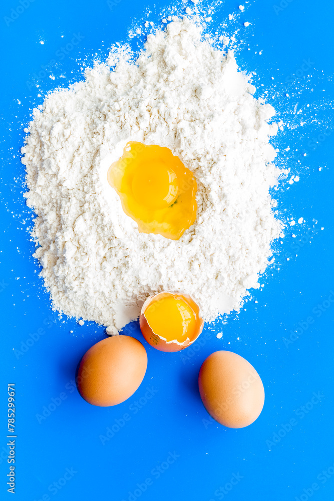 Making dough concept. Pile of flour and eggs on blue background top view Making dough concept. Pile of flour and eggs on blue background top view