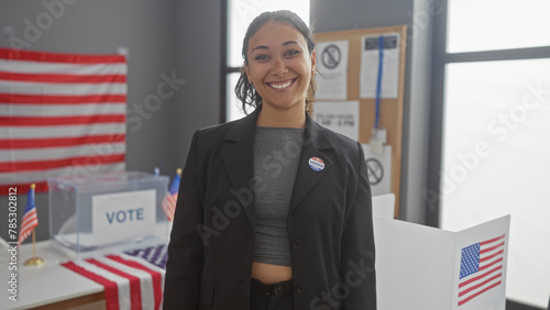 Smiling young hispanic woman with 'i voted' sticker at american electoral polling place with flags photo