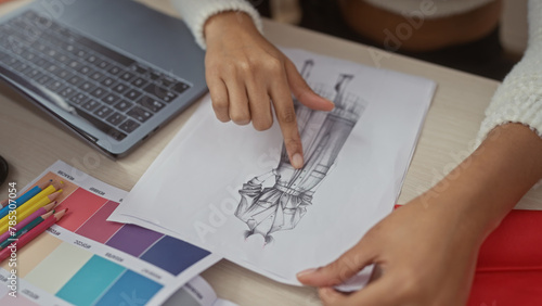 Woman and man collaborate in a tailor shop examining a dress sketch, surrounded by design tools and fabric swatches.