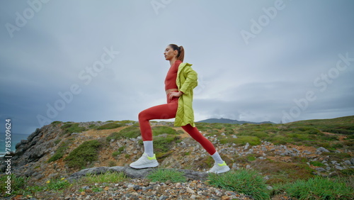 Fit woman stretching body at rugged coast. Sporty girl exercising cloudy nature