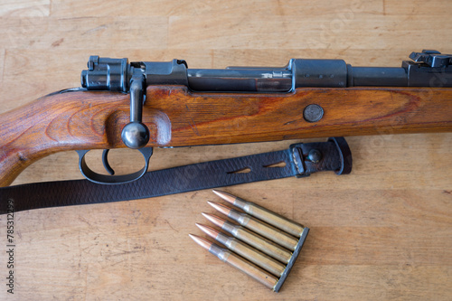 Detail of an ammunition clip with 5 30-06 caliber rifle bullets next to a Mauser-type bolt-action military rifle on a wooden table