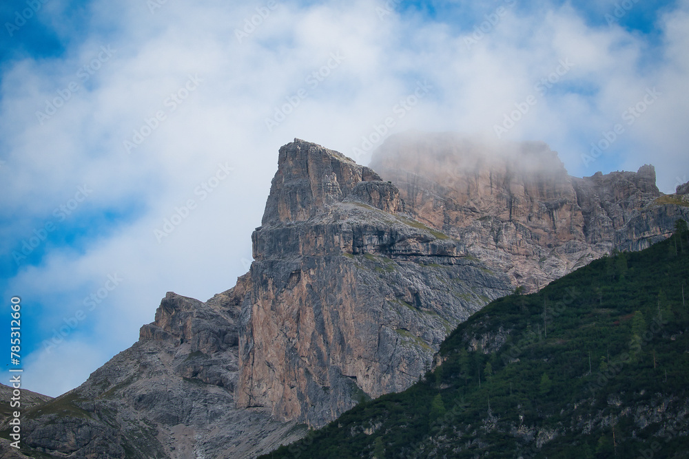 Ein spitz zulaufender Berggipfel, neben einem abgeflachten Gipfel in den südtiroler Dolomiten, eingehüllt in weisse Wolken