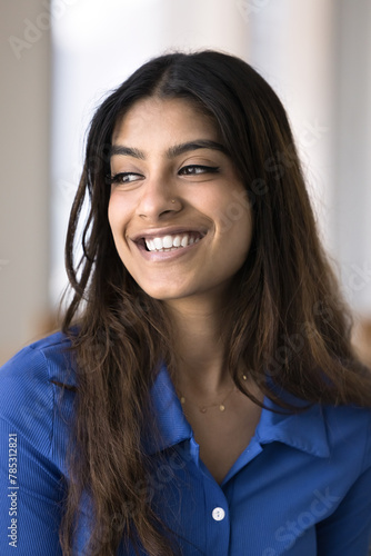 Positive attractive 20s Indian girl looking away with happy thoughts, smiling, laughing. Cheerful daydreaming beautiful young woman with nose stud and white teeth casual vertical portrait