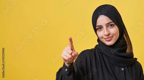 Hijab woman pointing at copy space over yellow background. Looking at camera. © Ajay