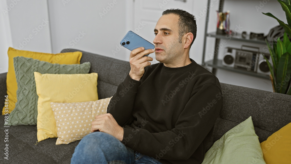 Hispanic man sending a voice message using his smartphone at home. Hispanic man sending a voice message using his smartphone at home.