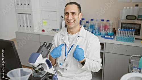 Smiling man in lab coat giving thumbs up in a laboratory with microscope and equipment
