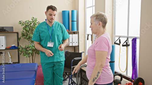 Man in scrubs interacts with woman by wheelchair in bright physiotherapy room photo