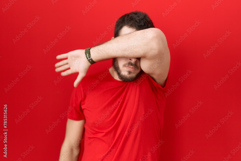Young hispanic man wearing casual red t shirt covering eyes with arm, looking serious and sad. sightless, hiding and rejection concept Young hispanic man wearing casual red t shirt covering eyes with arm, looking serious and sad. sightless, hiding and rejection concept