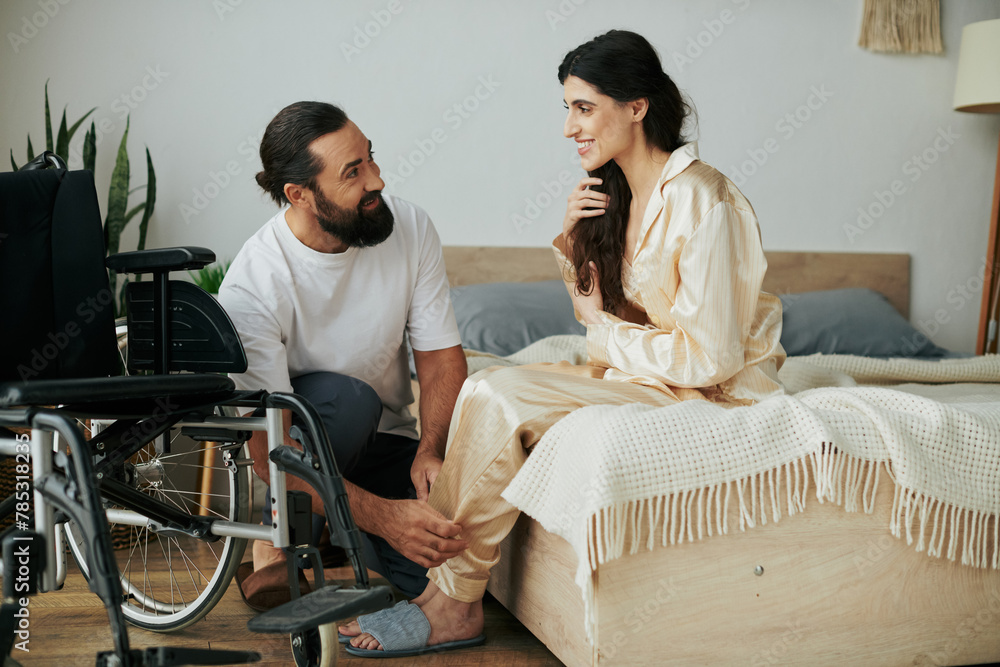 Obraz premium bearded loving man in homewear helping his disabled wife to change into pajama in bedroom at home