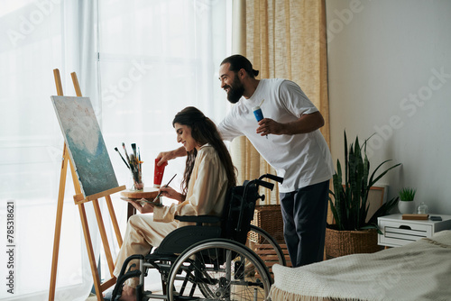 caring cheerful couple of bearded man and disabled woman painting on easel together at home photo