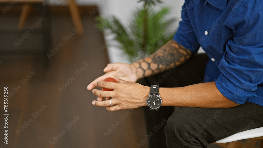 Tattooed hispanic man's hands, pressing an anti-stress ball while sitting in the waiting room
