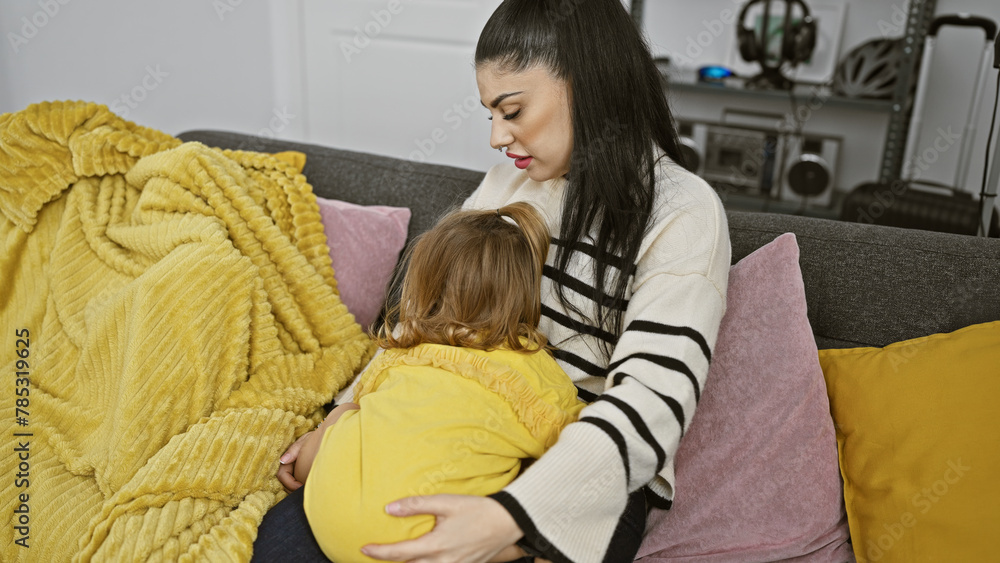 A tender moment as a woman hugs her young daughter, showing motherly love in a cozy indoor setting with colorful pillows.