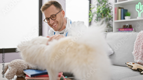 Confident young caucasian man vet happily examining a cute sick dog, smiling while sitting on the sofa at his cozy, indoors, home background
