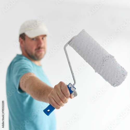 Young man holding a roller in front of himd - small depth of field.  The idea of painting the walls white.
