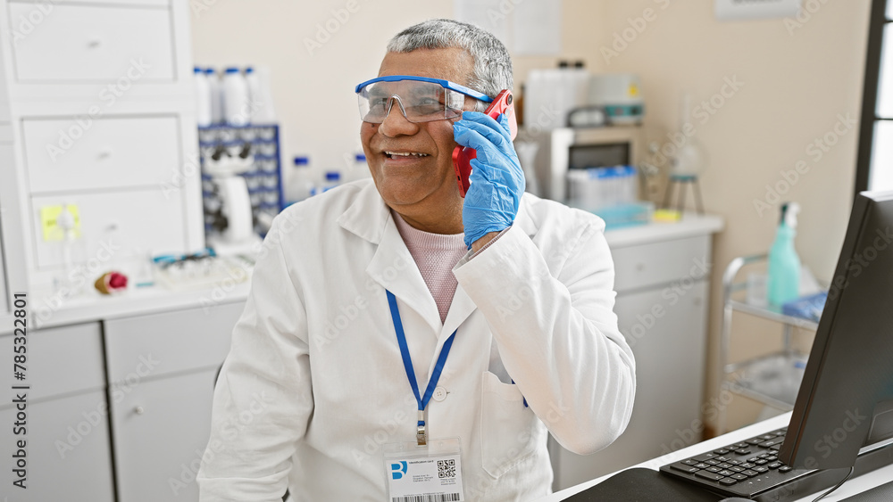 Smiling middle-aged man in lab coat talking on phone in laboratory Smiling middle-aged man in lab coat talking on phone in laboratory