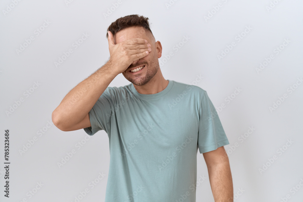 Hispanic man with beard standing over white background smiling and laughing with hand on face covering eyes for surprise. blind concept. Hispanic man with beard standing over white background smiling and laughing with hand on face covering eyes for surprise. blind concept.