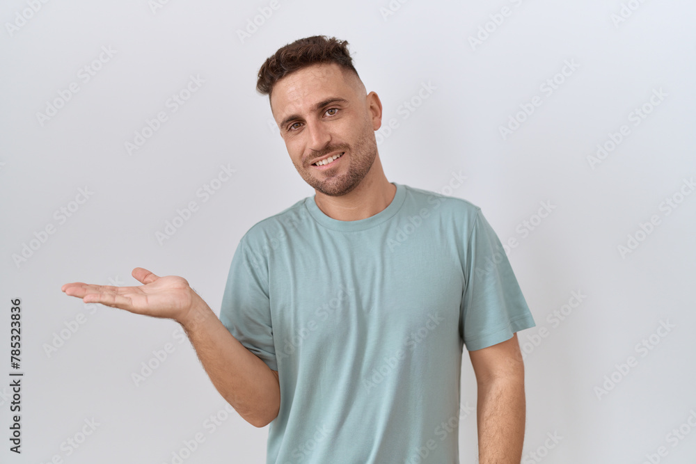 Hispanic man with beard standing over white background smiling cheerful presenting and pointing with palm of hand looking at the camera. Hispanic man with beard standing over white background smiling cheerful presenting and pointing with palm of hand looking at the camera.
