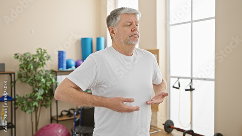Mature man practicing self-care exercises in a physiotherapy clinic room with a calm expression.