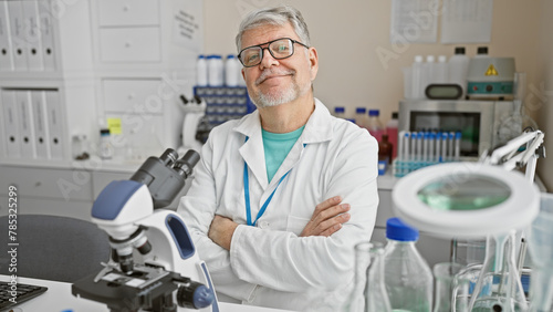 Confident male scientist with gray hair stands arms-crossed in a well-equipped laboratory indoors.