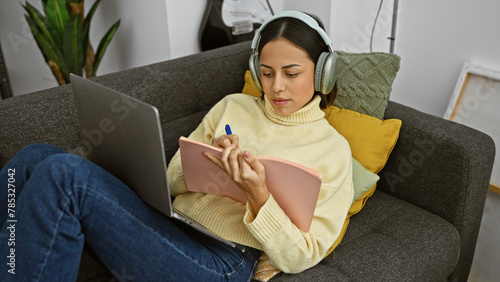 Tableau sur toile Hispanic woman studying with headphones and laptop on a couch indoors
