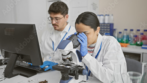 Man and woman scientists collaborate in a laboratory  with a microscope and samples while using technology.