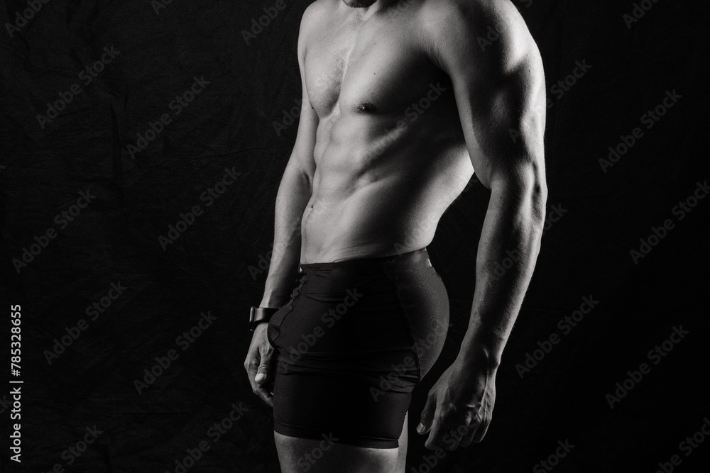 Man with exposed torso poses against black backdrop for flash photography