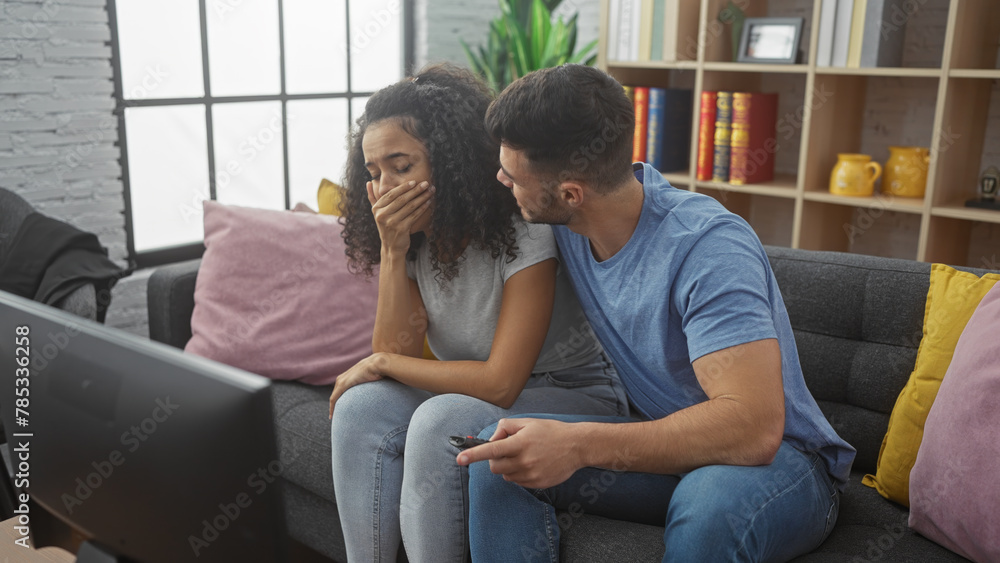 A concerned man comforting a woman on a sofa in a cozy living room while holding a remote. - obrazy, fototapety, plakaty 