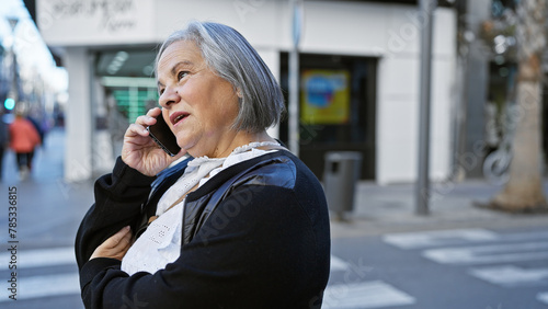 Senior woman conversing on mobile phone while standing on a busy city sidewalk.