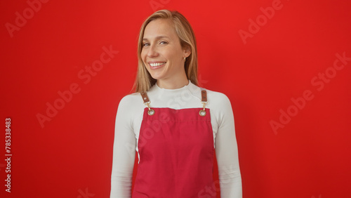 A smiling young caucasian woman in a red pinafore against an isolated red background exudes beauty and confidence. photo
