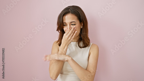 Young hispanic woman covering nose against a pink wall, showing disgust at a bad smell. photo