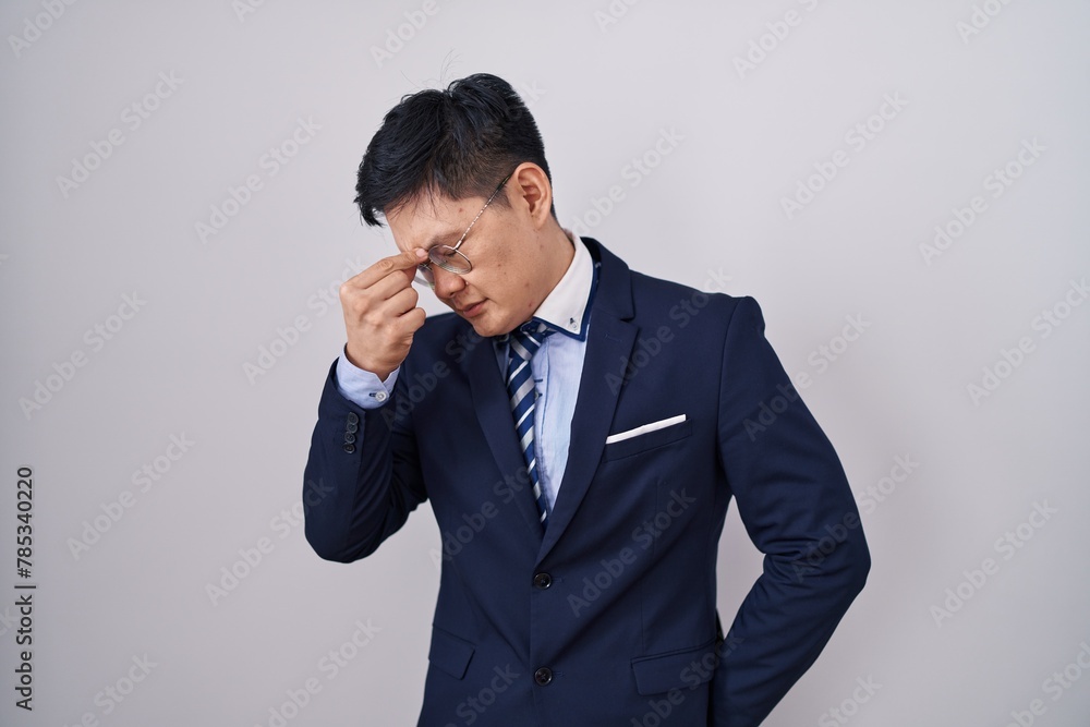 Young asian man wearing business suit and tie tired rubbing nose and eyes feeling fatigue and headache. stress and frustration concept.