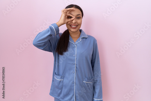 Young arab woman wearing blue pajama doing ok gesture with hand smiling, eye looking through fingers with happy face. © Krakenimages.com