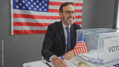 Smiling mature man in suit casting ballot with american flag backdrop inside voting center.