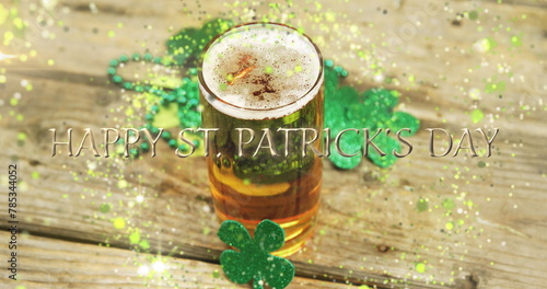Image of st patrick's day text, shamrock and glass of beer on wooden background