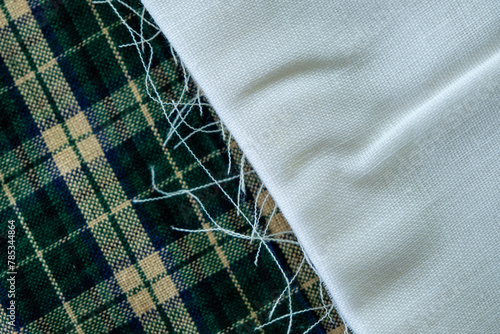 Folded white fabric with frayed edge on top of green plaid