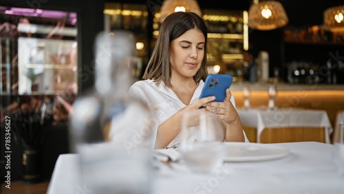 Young beautiful hispanic woman smiling happy using smartphone sitting on the table at the restaurant © Krakenimages.com