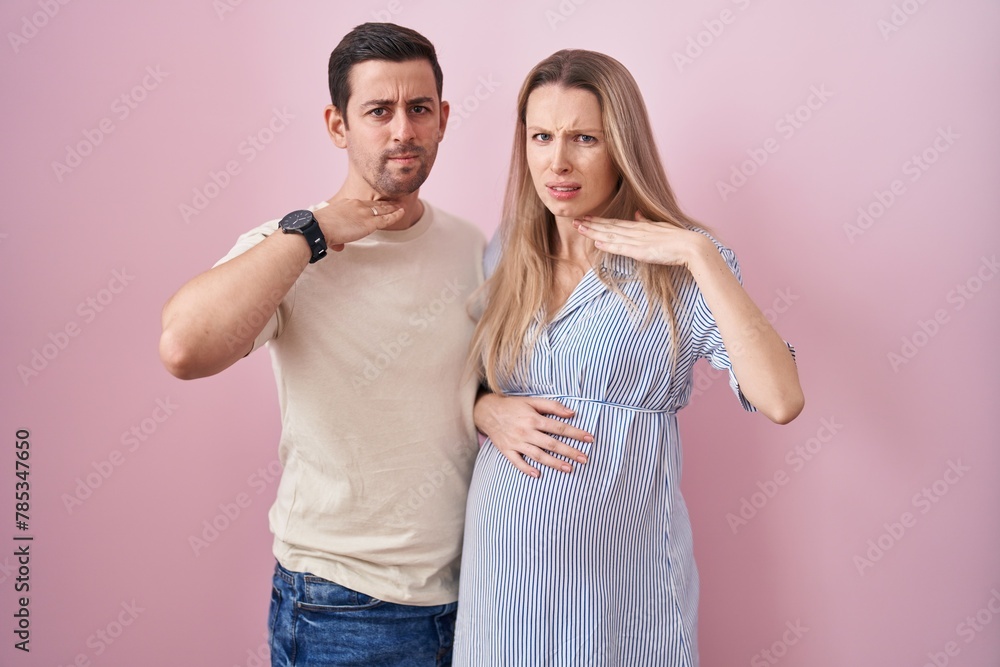 Young couple expecting a baby standing over pink background cutting throat with hand as knife, threaten aggression with furious violence Young couple expecting a baby standing over pink background cutting throat with hand as knife, threaten aggression with furious violence