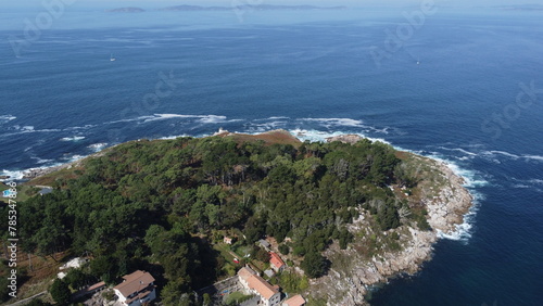 Serene coastal landscape featuring a small mountain enveloped by the sea, framed by lush greenery and rocky shores