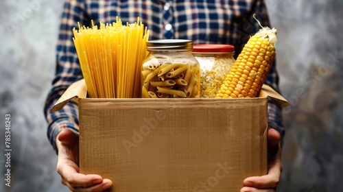 A person holding an open cardboard box filled pasta and corn. photo