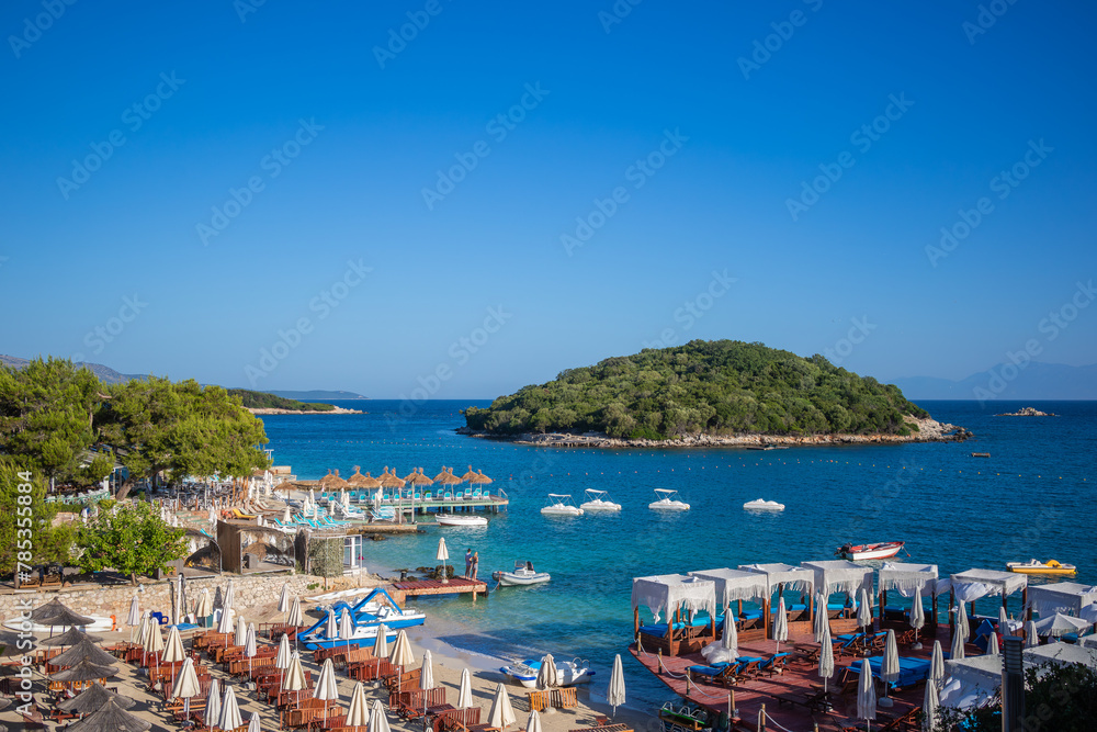Beach Vacation in Sunny Southern Albania. Beautiful Day Scenery of Ksamil Island, Ionian Sea, Sandy Shore, Piers with Sunbed in Albanian Riviera.
